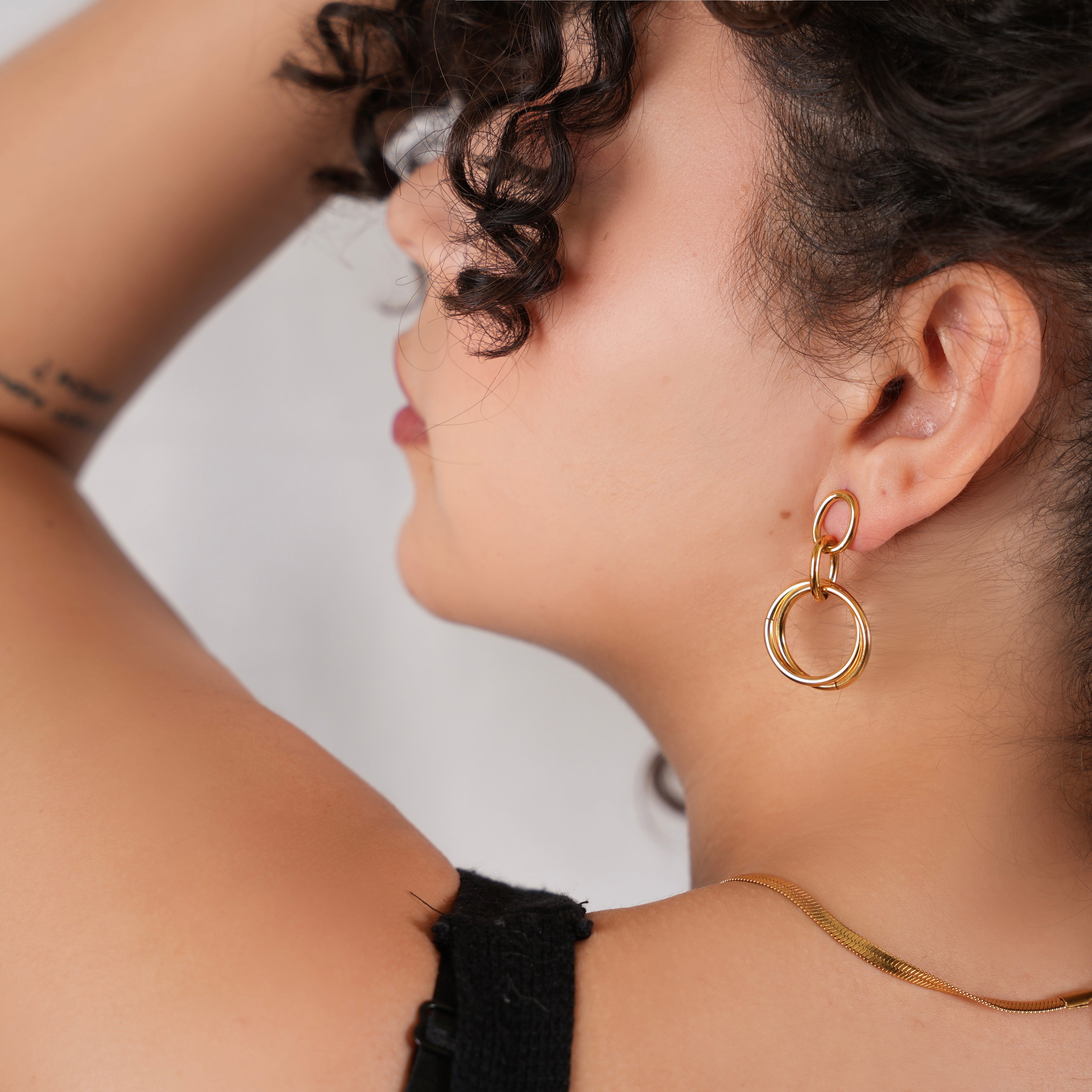 Close-up of a woman wearing gold hoop earrings with a neutral background
