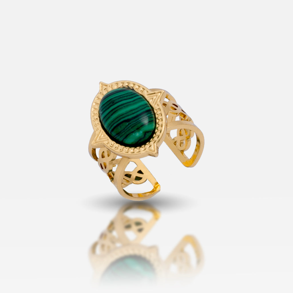 A gold-colored adjustable ring with a large green emerald-like stone in the center, surrounded by intricate detailing.