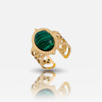 A gold-colored adjustable ring with a large green emerald-like stone in the center, surrounded by intricate detailing.