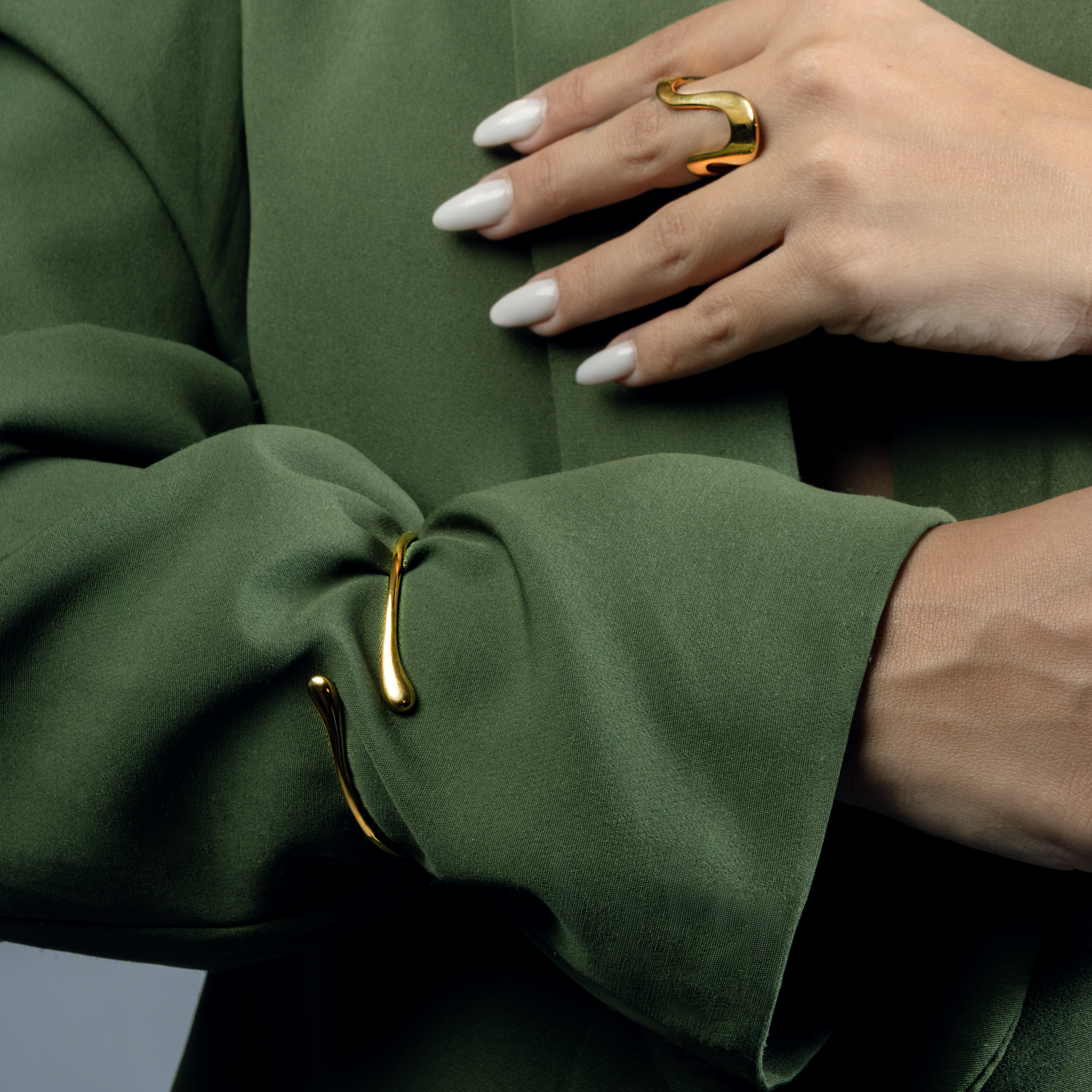 Close-up of a hand wearing a gold ring on a green garment with gold buttons.