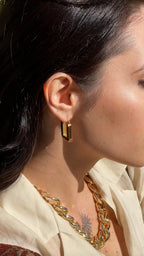 Close-up of a person wearing gold earrings and a necklace with a soft focus background