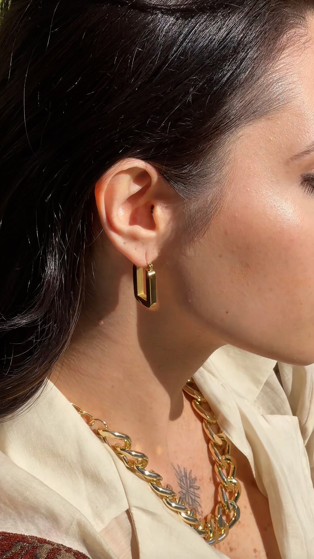 Close-up of a person wearing gold earrings and a necklace with a soft focus background